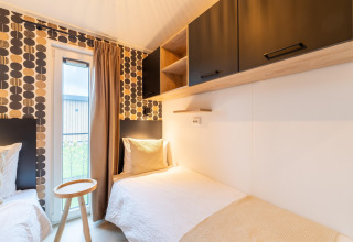 Helles Schlafzimmer mit zwei Einzelbetten, kreativer Tapete und schwarzen Schränken in der Lodge «By the Baker» in den Niederlanden.
