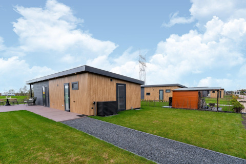 Moderne Holzlodge bei By the Baker in den Niederlanden mit gepflegtem Rasen und sonnigem Himmel.