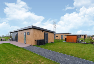 Modern wooden lodge at By the Baker in the Netherlands, featuring green lawns and a bright blue sky.