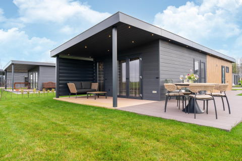 Modern lodge at 'By the Baker' in the Netherlands with terrace, outdoor seating and garden on a cloudy day.