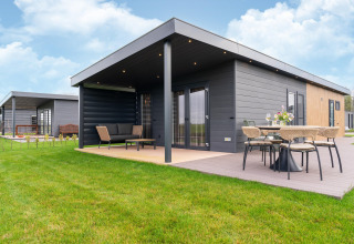 Moderne Lodge bei 'By the Baker' in den Niederlanden mit überdachter Terrasse, Gartenmöbeln und Rasen.