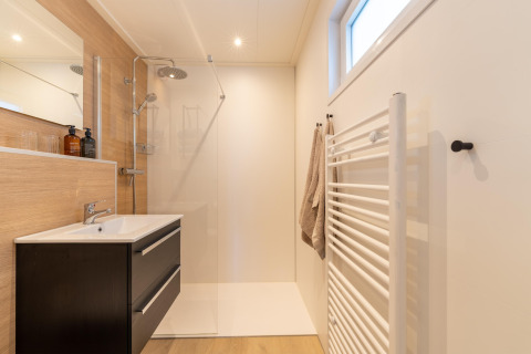 Modern minimalist bathroom with walk-in shower, vanity, and towel radiator at 'By the Baker' lodge in the Netherlands.
