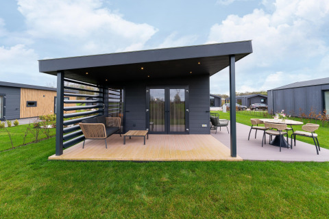 Modern lodge with covered terrace and outdoor seating at By the Baker in the Netherlands, set in green lawns.