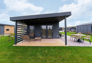 Modern lodge with covered terrace and outdoor seating at By the Baker in the Netherlands, set in green lawns.
