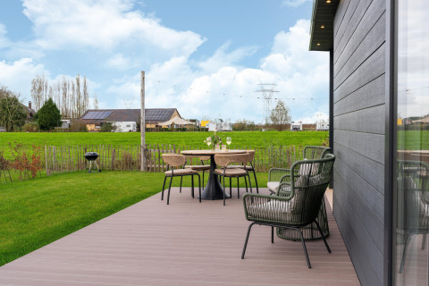 View from By the Baker lodge with deck, garden furniture, and green fields in the Netherlands.
