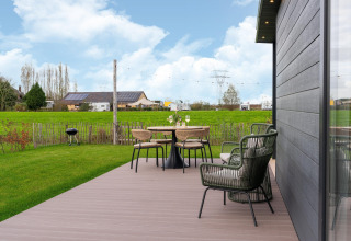 View from By the Baker lodge with deck, garden furniture, and green fields in the Netherlands.