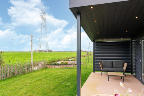 View from the terrace at ‘By the Baker’ lodge in the Netherlands, featuring green fields and open sky.