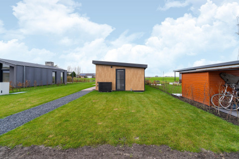 Modern wooden lodge with green lawn and bicycle shelter at By the Baker in the Netherlands.