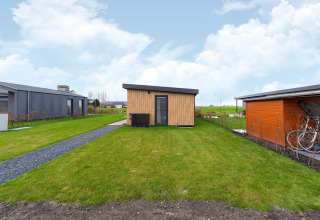 Modern wooden lodge with green lawn and bicycle shelter at By the Baker in the Netherlands.