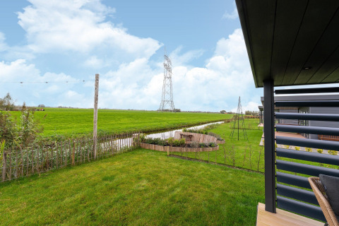 View from the lodge 'By the Baker' in the Netherlands, showing garden, fields, a canal and power lines.