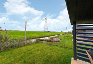 View from the lodge 'By the Baker' in the Netherlands, showing garden, fields, a canal and power lines.