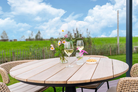 Outdoor table at 'By the Baker' lodge in the Netherlands with wine, flowers, and snacks under blue sky.