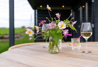 Outdoor table with vase of flowers, wine glass, and drinks at By the Baker lodge in the Netherlands.