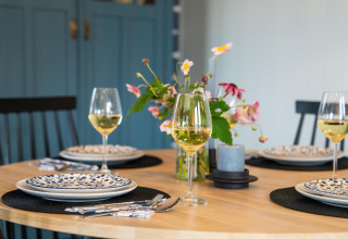 Elegant gedeckter Tisch mit Weingläsern, Blumen und blauen Schränken im 'By the Baker' Lodge in den Niederlanden.