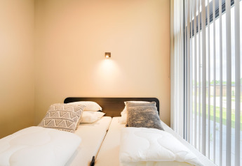 Camera moderna con due letti singoli, cuscini decorativi e ampia finestra presso Holiday home vicino ai laghi Kaag, Paesi Bassi.