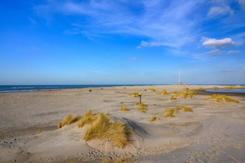 Plage avec dunes et herbes près d’un hébergement glamping, quelques personnes marchant au loin.
