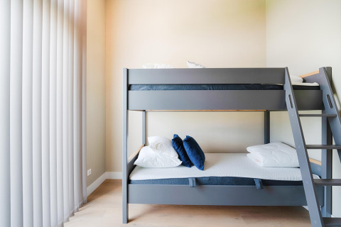Lit superposé moderne avec coussins bleus et blancs dans une chambre lumineuse avec grands stores verticaux.