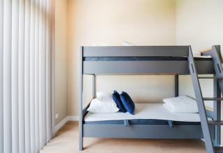 Lit superposé moderne avec coussins bleus et blancs dans une chambre lumineuse avec grands stores verticaux.