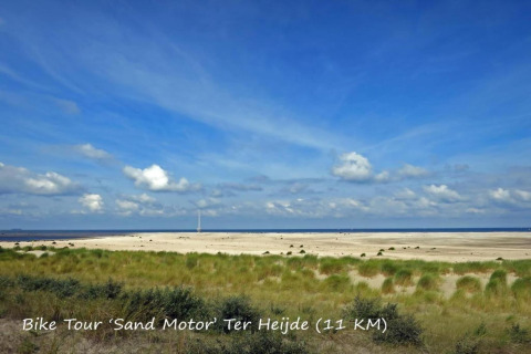 View of the Sand Motor near Ter Heijde with grass, dunes, and sea under a blue sky at a glamping site.