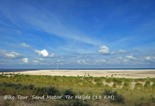 View of the Sand Motor near Ter Heijde with grass, dunes, and sea under a blue sky at a glamping site.