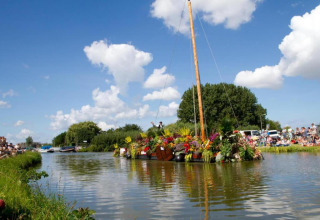 Un radeau fleuri passe devant des spectateurs sur un canal lors d'une journée ensoleillée au glamping.