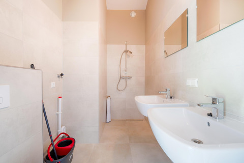 Salle de bain lumineuse avec deux lavabos, douche et matériel de nettoyage près des lacs Kaag aux Pays-Bas.