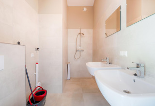 Salle de bain lumineuse avec deux lavabos, douche et matériel de nettoyage près des lacs Kaag aux Pays-Bas.