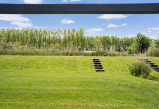 Vue sur pelouse verte, marches et arbres sous ciel bleu près des lacs Kaag à une maison de vacances aux Pays-Bas.