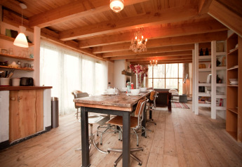 Knusse houten eetruimte in De Schone Leij hut, Nederland, met rustieke meubels en grote vensters.