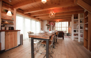 Cozy wooden cabin dining area at De Schone Leij in the Netherlands, featuring rustic furniture and large windows.