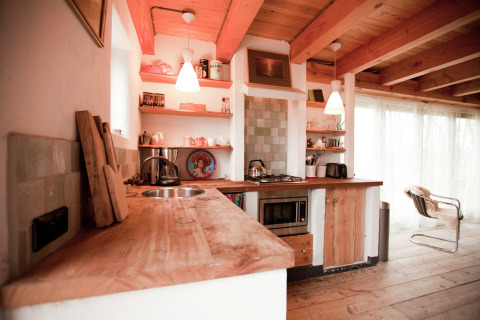 Rustieke houten keuken met open planken, moderne apparatuur en warm licht in een Nederlandse cabin.