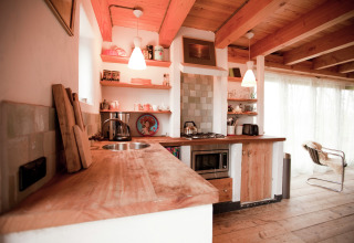 Rustieke houten keuken met open planken, moderne apparatuur en warm licht in een Nederlandse cabin.