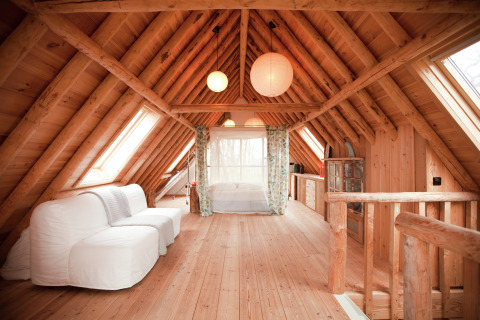 Knus zolderinterieur met houten balken en witte bank in De Schone Leij cabin in Nederland.