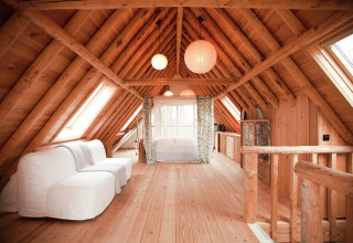 Knus zolderinterieur met houten balken en witte bank in De Schone Leij cabin in Nederland.