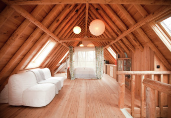 Wooden attic interior with white sofa, bed, skylights at De Schone Leij cabin in the Netherlands.