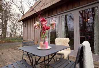 Buitenterras aan het huisje 'De Schone Leij' in Nederland met tafel, stoelen, bloemen en kaarsen.