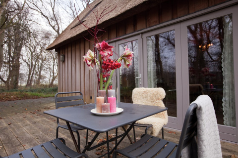 Buitenterras bij hut 'De Schone Leij' in Nederland, met tafel, stoelen, bloemen en kaarsen.
