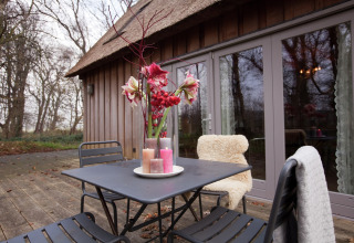 Buitenterras bij hut 'De Schone Leij' in Nederland, met tafel, stoelen, bloemen en kaarsen.