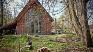 Photo of the De Schone Leij cabin with large glass windows, surrounded by trees and natural scenery.
