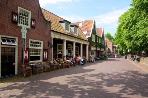 Mensen zitten buiten bij café De Schone Leij in een schilderachtig Nederlands dorp, zonnige dag.