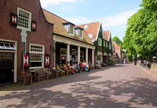 Mensen zitten buiten bij café De Schone Leij in een schilderachtig Nederlands dorp, zonnige dag.