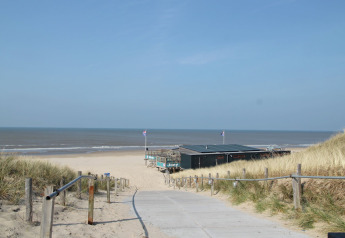 A path through sandy dunes leads to the cabin De Schone Leij on a sunny beach in the Netherlands.