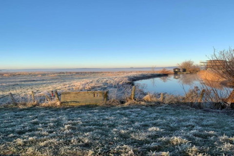 Bevroren veld met vijver bij de hut ‘De Schone Leij’ onder een heldere lucht in Nederland.
