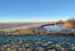 Bevroren veld met vijver bij de hut ‘De Schone Leij’ onder een heldere lucht in Nederland.