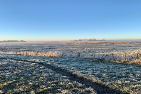Bevroren veld bij het huisje De Schone Leij in Nederland onder een heldere blauwe lucht.