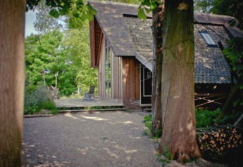 The cabin De Schone Leij in the Netherlands, surrounded by lush trees and nature on a sunny day.