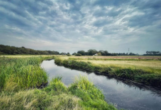 Landschap bij het huisje 'De Schone Leij' in Nederland met beek, grasland en bewolkte lucht.