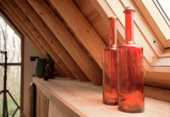 Twee rode glazen flessen op een houten plank in een gezellige hut met schuin raam in Nederland.