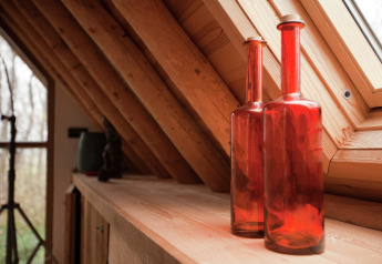Two red glass bottles sit on a wooden shelf in a cozy cabin with slanted windows and exposed beams in the Netherlands.