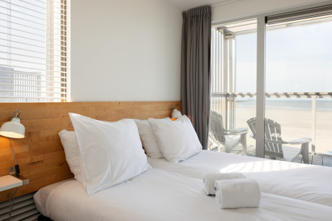 Helles Schlafzimmer mit Doppelbett, Kissen und Balkon mit Meerblick im Resort Hoek van Holland, Niederlande.